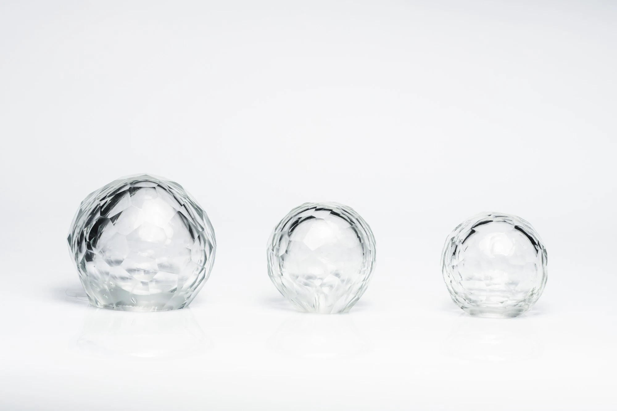 Three clear faceted blown glass spheres of decreasing size in a row on a white surface