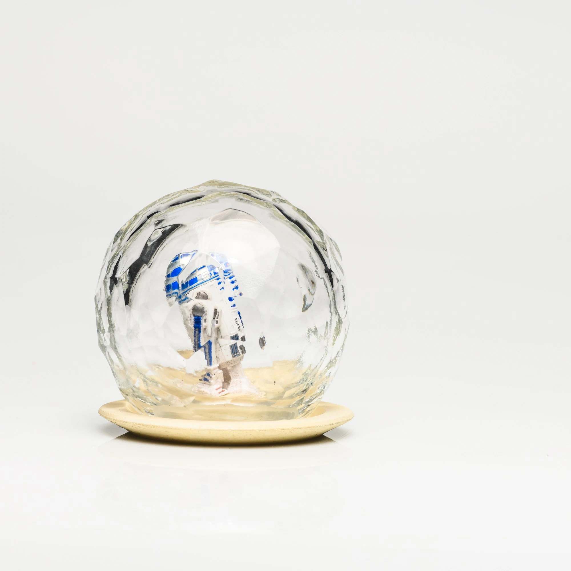 Faceted blown glass dome enclosing a white and blue toy figure, on a pale round pedestal