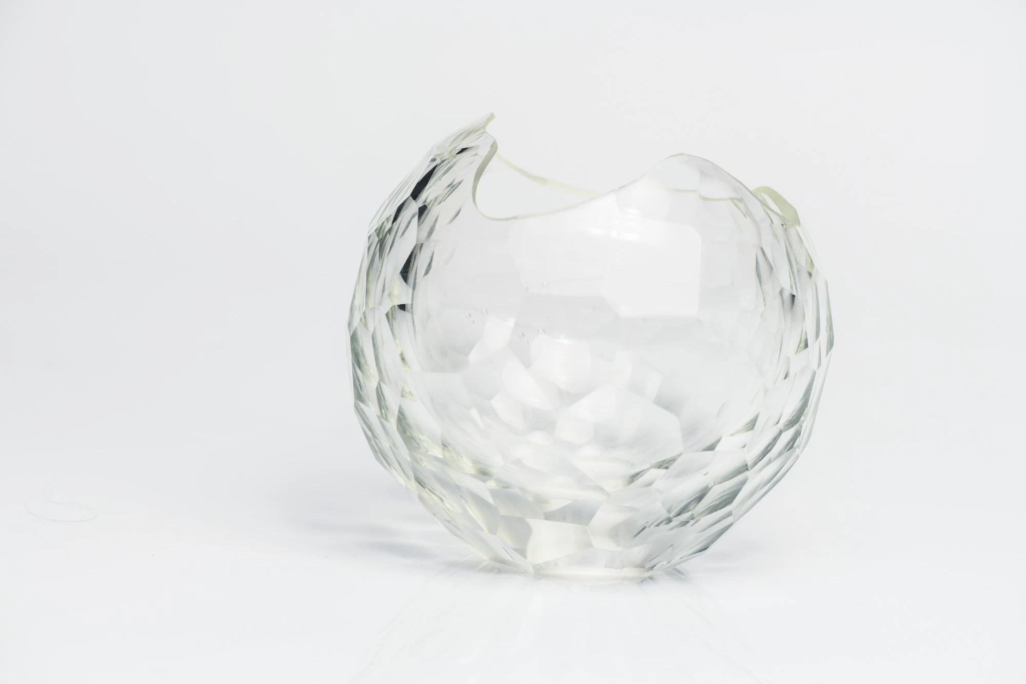 Clear faceted blown glass form, broken open at the top, on a white surface