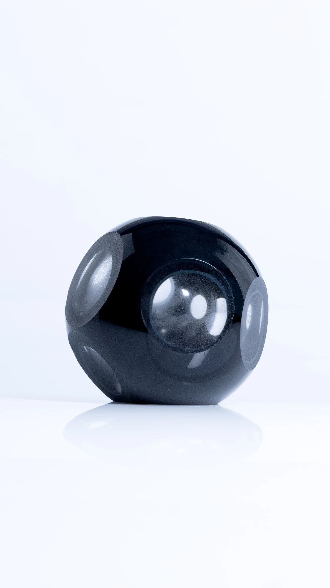 Black glass sphere cut with round polished windows, on a white surface