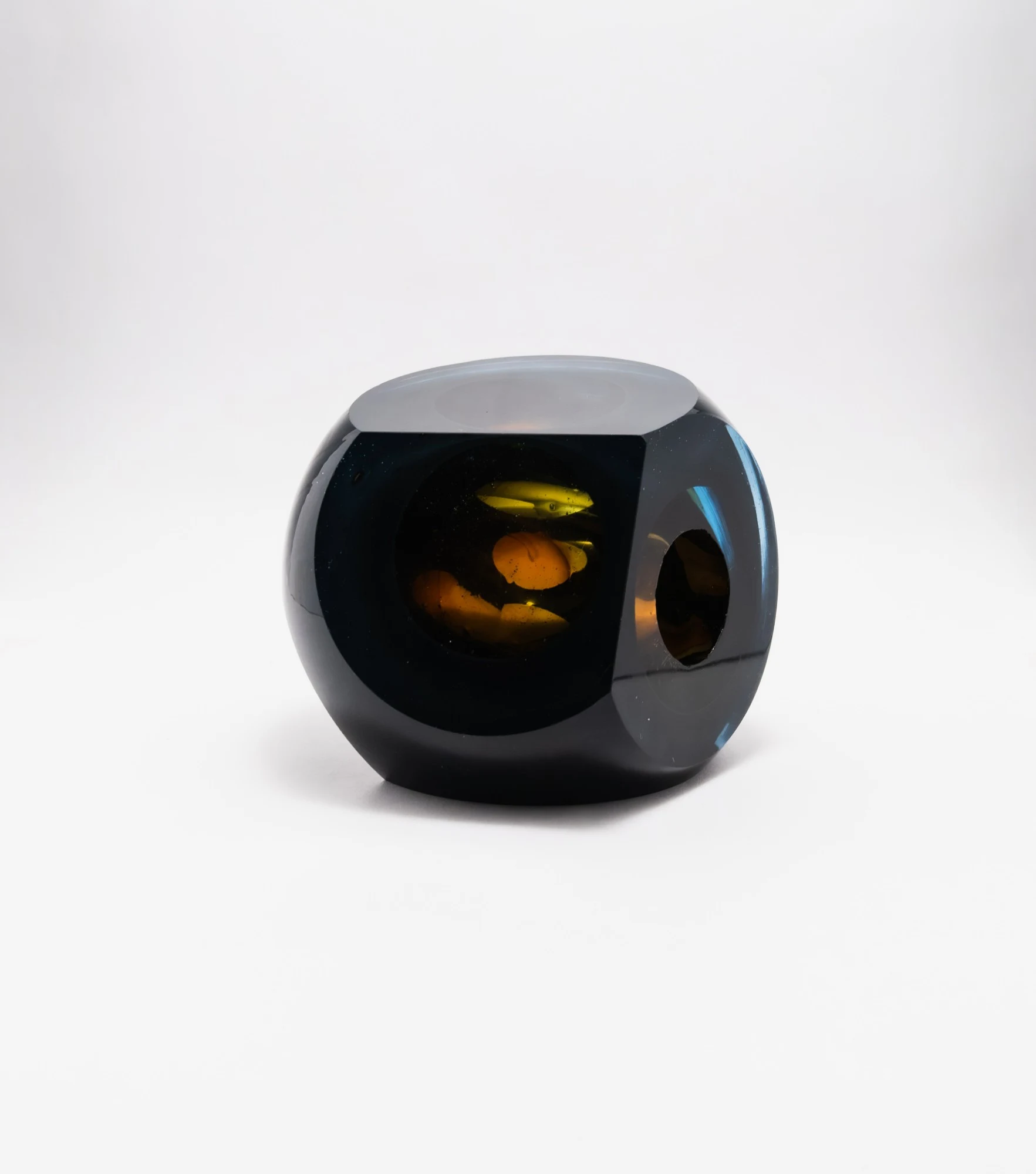 Dark blue-black cut glass form with amber shapes inside, seen through a large polished window