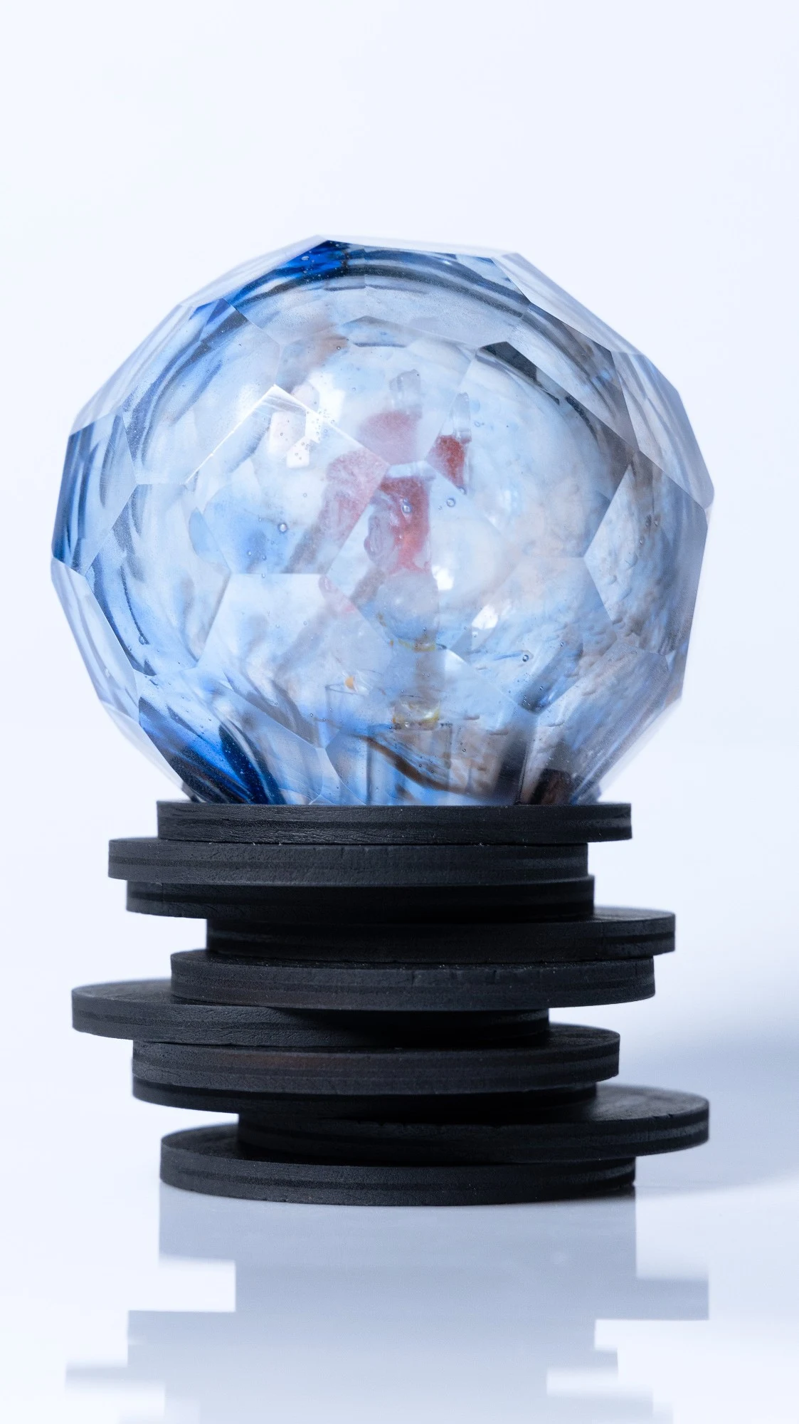 Faceted glass sphere with blue and white glass and a red cast form inside, on a stack of black plywood discs