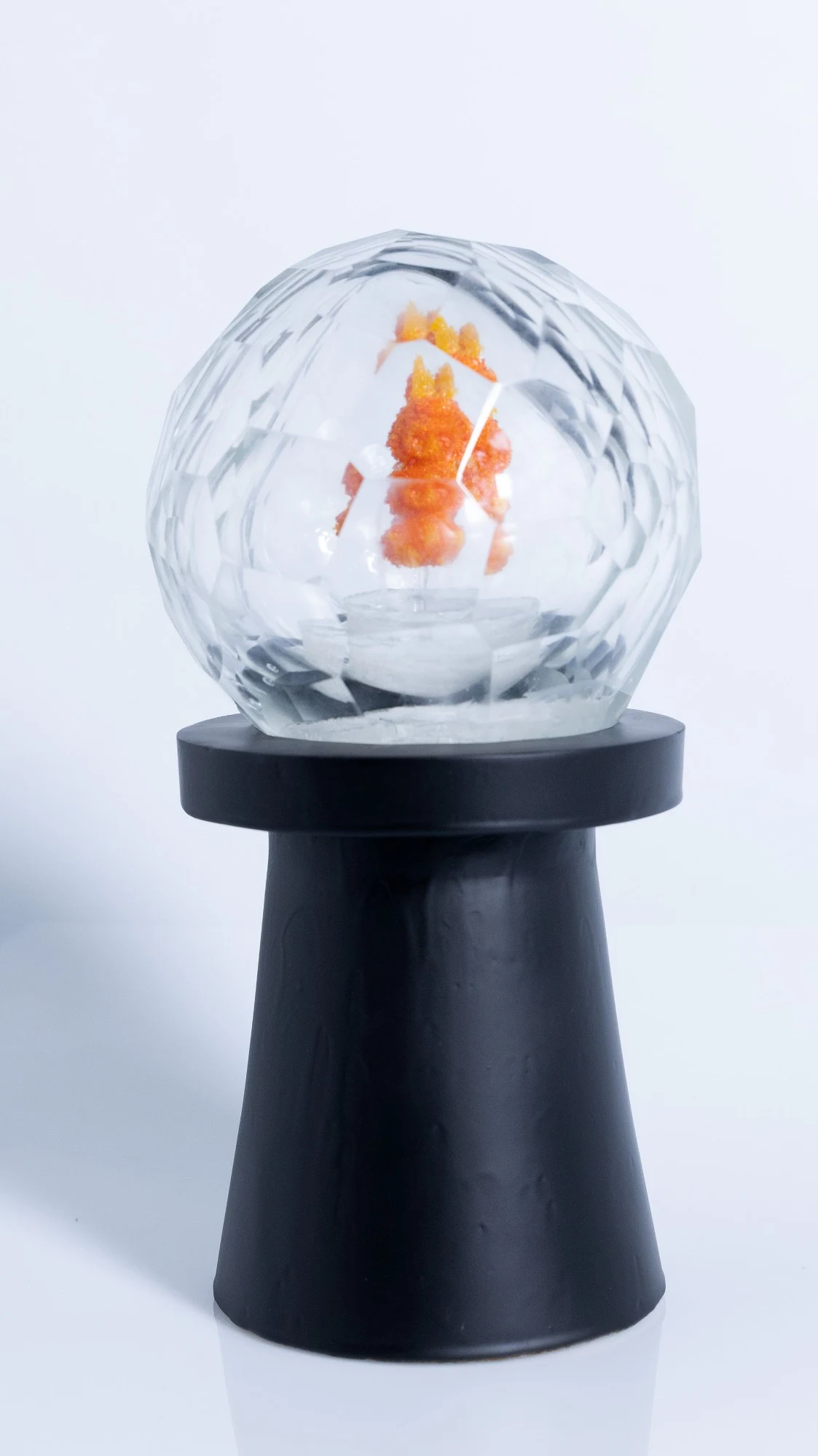 Faceted glass sphere with an orange pâte de verre figure inside, on a tall black plaster pedestal